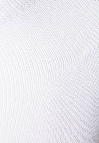 Weißer gerippter Stoff mit einer strukturierten Oberfläche, die feine horizontale und vertikale Linien zeigt, typisch für Strickmaterial.