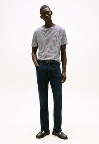Tricou gri cu dungi, prevăzut cu un buzunar, blugi negri, curea neagră și pantofi de tip loafer negri. Ținuta are un design casual, ajustat.