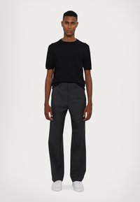 Svart t-skjorte med korte ermer kombinert med skreddersydde grå bukser og hvite joggesko. Enkel design, nøytrale farger, glatt tekstur.
