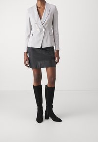 Blazer doppiopetto grigio chiaro attillato con bottoni dorati, abbinato a una minigonna in pelle nera e stivali alti fino al ginocchio in suede nera.