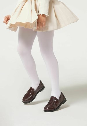 Braune Lacklederschuhe mit einer niedrigen schwarzen Sohle, getragen mit weißen Strumpfhosen unter einem beigen Kleid, das einen ausladenden Rock und gerippte lange Ärmel hat.