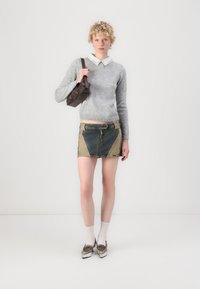 Pulover tricotat gri, cămașă albă cu guler și nasturi, fustă mini din denim în nuanțe de albastru și bej, asortată cu mocasini argintii și șosete scurte. Geantă de umăr maro.