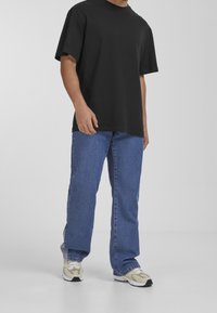 Black short-sleeve t-shirt paired with light blue straight-leg jeans and beige sneakers with white soles, standing against a neutral background.