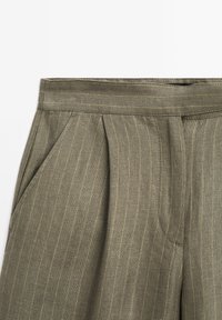 Khaki w paski spodnie z zakładkami, z bocznymi kieszeniami i gładką teksturą. Materiał ma subtelne żółte pionowe linie.
