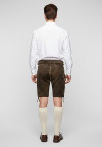 Hnědé kožené šortky, bílá dlouhá košile a krémové podkolenky. Hnědé boty dokončují outfit. Jednoduchý, funkční design.