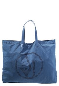 Niebieska torba na ramię z dwoma uchwytami, z dużym, ciemnym logo w okrągłym wzorze. Materiał wydaje się teksturowany i lekki.