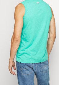 Camiseta sin mangas de color verde menta, hecha de un tejido ligero, con un escote redondo y un corte holgado, combinada con jeans azules.