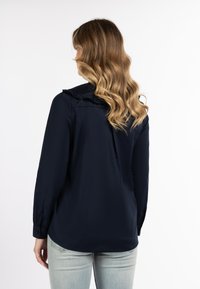 Marineblå skjorte med knapper og flæsekrave samt lange ærmer, lavet af glat stof, båret med lyseblå jeans.