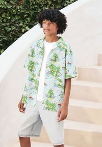 Chemise à manches courtes bleu clair avec imprimé de palmiers et océan, associée à un short en denim clair. Tissu doux, coupe décontractée, palette de couleurs vive.