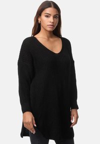 Schwarzer Strickpullover mit V-Ausschnitt, langen Ärmeln und lockerer Passform. Strukturiertes Gewebe mit gerippten Details und Seitenschlitzen am Saum.