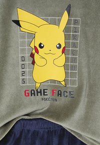 Gelber Pikachu mit entschlossenem Ausdruck steht vor einem Gitterhintergrund mit den Texten "0025", "Pikachu" und "Game Face Pokémon".