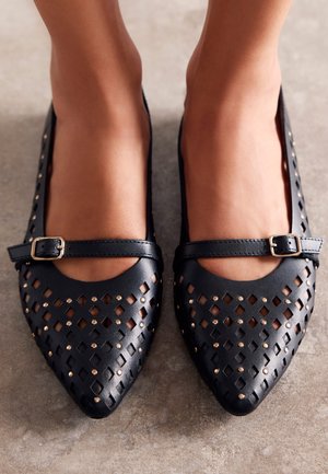 Ballerine in pelle nera con design perforato, punte appuntite e una sottile tracolla con fibbia. Accentuate da piccoli chiodini d'oro.