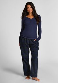 Marineblauwe longsleeve met knoopdetails, gecombineerd met een geruite broek in donkerblauw, groen en gele accenten; losse pasvorm, zachte textuur.