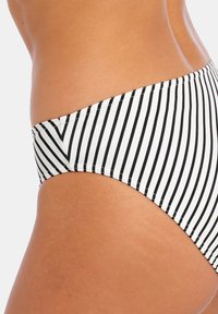 Bikini inferior a rayas blancas y negras, diseño contorneado, tela elástica, con corte bajo y textura suave. Detalle de rayas horizontales.