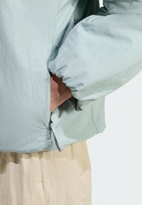 Svetlomodrá, textúrovaná bunda s elastickými manžetami. Má bočnú zipsovú kapsu. Nosí sa cez krémový, ľahký odev.