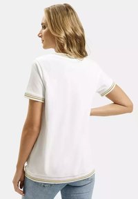 Biała koszulka polo z krótkim rękawem, z złotymi i zielonymi paskami na kołnierzyku i rękawach, z prostym dołem i luźnym krojem.