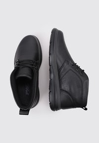 Zapatos de cuero negro con una textura suave, punta redondeada y diseño de tobillo bajo. Los cordones y los sutiles detalles de costura mejoran la funcionalidad.