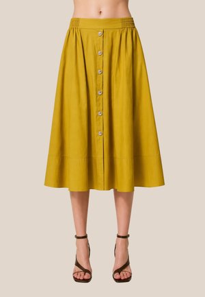 Gonna midi gialla con bottoni frontali e vita elasticizzata arricciata, indossata con sandali con cinturini e tacco alto marrone scuro.