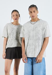 Grå, tie-dye t-skjorter med kort erme og avslappet passform; kombinert med et svart plisserte skjørt og blå denimshorts.