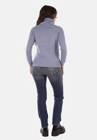 Maglione a collo alto blu chiaro con polsini a coste, abbinato a jeans di denim scuro e stivali neri chunky, che mostrano una texture semplice e liscia.