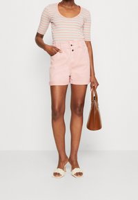 Raidallinen, lyhythihainen bodytoppi, jossa on avonainen kaula-aukko, yhdistettynä vaaleanpunaiseen korkeavyötäröiseen shortsipariin, jossa on käänteet ja etunapit.