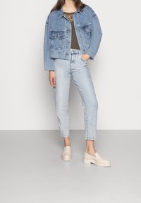 Giacca di jeans in blu chiaro, con tasche a toppa e orlo sfilacciato. Abbinata a jeans blu chiaro e mocassini con zeppa beige.