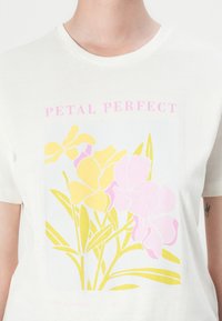 Bílé bavlněné tričko s botanickým potiskem, na kterém jsou žluté a růžové květy, text "PETAL PERFECT" a zelené listy v obdélníkovém designu.