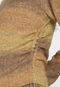 Pulôver de malha em gradiente castanho e amarelo com detalhe franzido lateral, apresentando uma textura suave e bainha canelada.