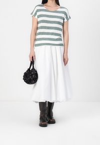 Top de rayas verdes y blancas de manga corta, combinado con una falda blanca y vaporosa. Bolsa negra con patrón floral y botas marrones hasta la rodilla.