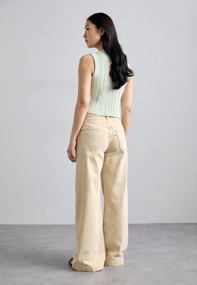 Top court côtelé vert clair avec une découpe dans le dos, associé à un pantalon large beige, vu de dos.
