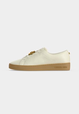 Biały niski sneaker z skóry z beżową podeszwą, złotym logo MICHAEL KORS po boku i złotym dekoracyjnym emblematem na sznurowadłach.