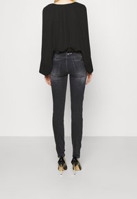 Musta pitkähihaine paita yhdistettynä tummanharmaisiin tiukkoihin farkkuihin. Farkuissa on teksturoitu vyötärönauha koristeilla ja terävät mustat korot.