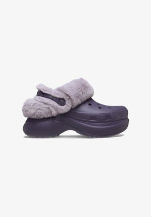 Purple molded clogs with a faux fur cuff, featuring ventilation holes, a textured sole, and an adjustable strap for a secure fit.