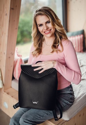 Schwarzer Leder-Rucksack mit gesteppter Klappe, featuring ein Emblem-Detail am Boden und verstellbaren Trägern. Glatte Textur, modernes Design.