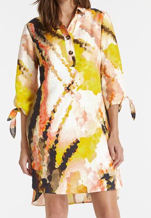 Femme portant une robe à imprimé abstrait multicolore avec manches trois-quarts nouées aux poignets et col en V boutonné.