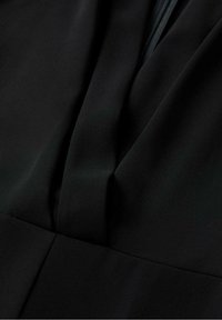 Zwarte stof close-up, met een zachte textuur en subtiele draping. Het ontwerp bevat plooien en een V-vormige halslijn detaillering.