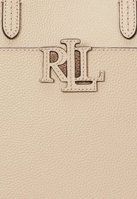Bežová kožená taška s vyrazeným logom "RL" v kontrastnom odtieni, s hladkou textúrou a detailne prešitými akcentmi.