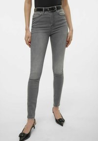 Jeans ajustados grises de denim con una textura suave, que cuentan con bolsillos frontales y una cintura alta, combinados con zapatos negros de punta.