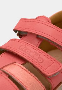 Πέδιλα από κοραλλί δέρμα με δύο λουριά βέλκρο και επενδεδυμένη εσωτερική επιφάνεια. Ραφές με λεπτομέρειες και ανάγλυφο λογότυπο στο λουράκι. Λείος υφής.