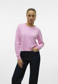 Pullover rosa a maglia con scollatura a girocollo e maniche lunghe, abbinato a jeans in denim blu scuro. Il tessuto appare morbido e leggero.