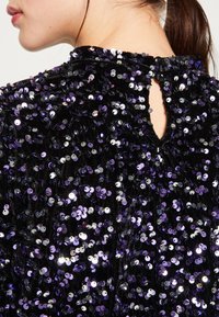 Indumento nero con paillettes, dotato di paillettes tonde viola e argento, superficie testurizzata e una piccola apertura a forma di chiave sul retro.