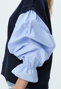 Maglione con corpo blu navy e maniche a sbuffo di un blu chiaro, realizzate in cotone. Le maniche presentano polsini arriccivati e una trama liscia.