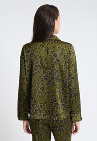 Groene blouse met een losvallende pasvorm, met zwarte bloemvormen en accenten. Een gladde textuur en lange mouwen maken het ontwerp compleet.