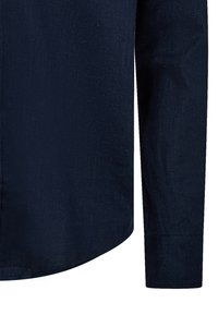 Navyblauwe langarmshirt van textuurstof; heeft een puntige kraag en een afgeronde onderkant met knoopmanchetten.