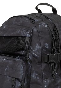 Svart ryggsäck med en strukturerad tyg, med ett subtilt metalliskt mönster, dragkedjor, nätficka och hållbara justerbara axelremmar.