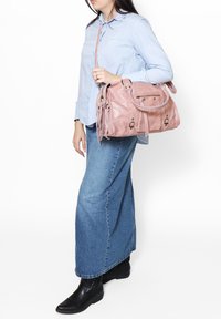 Sac à main en cuir rose avec poignées supérieures et bandoulière, présentant des zips et des détails en franges. Une texture lisse avec des accents métalliques.