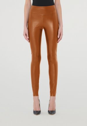 Bruine nepleer legging met een hoge taille en een gladde, glanzende textuur, gecombineerd met zwarte hoge hakken.