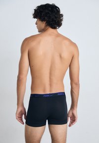 Schwarze Nike-Boxershorts mit lila Bund, aus weichem Stoff und passgenauer Ausführung, von hinten gegen einen neutralen Hintergrund betrachtet.