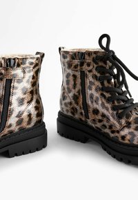 Paire de bottines marron imprimé léopard avec lacets noirs, fermetures éclair latérales et semelles épaisses en caoutchouc noir sur fond blanc.