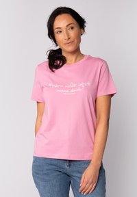 Roze katoenen T-shirt met korte mouwen, met witte tekst die op de voorkant staat: "Wenn nicht jetzt, wann dann?". Klassiek ronde hals ontwerp.